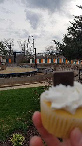 Mary Kwiatkowski holds a Pantheon cupcake in front of the new coaster at Busch Gardens Williamsburg.