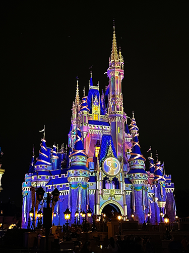 Cinderella Castle all lit up at night with projections for the Beacons of Magic at the Magic Kingdom.